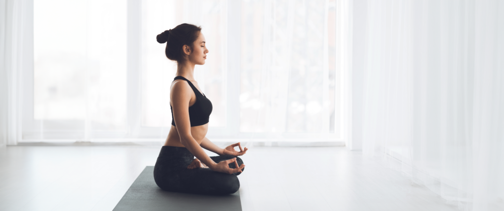 Eine Frau sitzt in typischer Yoga Pose auf dem Boden.